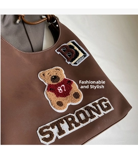 Dettaglio borsa tote in pelle marrone con toppa orsetto e ricami vintage stile varsity