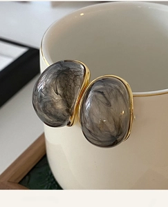Macro view of oval resin earrings with gold trim and gray marble texture on white ceramic