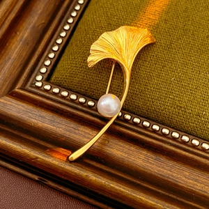 Close-up of gold plated ginkgo leaf brooch with white pearl on vintage frame