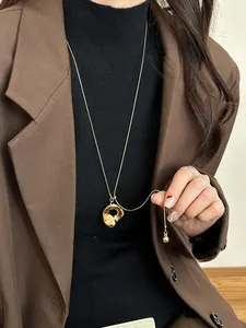 Irregular organic circle pendant on a long gold lariat chain necklace over a brown blazer