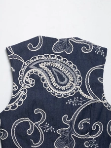 Detailed macro of white paisley embroidery on dark blue denim fabric texture