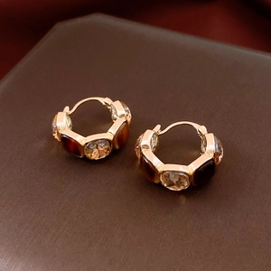 Close-up of golden U-shaped earrings with square resin stones on a dark surface