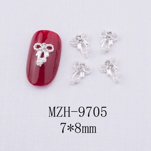 Détail de breloque nœud argenté pour ongles avec perles blanches et strass sur ongle rouge