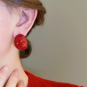 Close-up of elegant red button stud earrings worn by a model in a red sweater