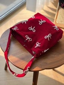 Detail of red corduroy tote bag featuring white bow embroidery on a wooden stool