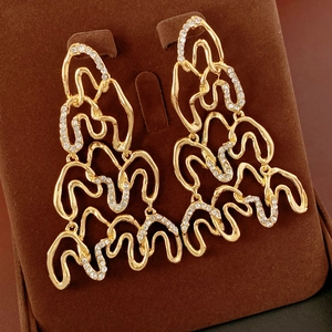 Close-up of golden wavy hollow earrings with shimmering rhinestones on dark velvet