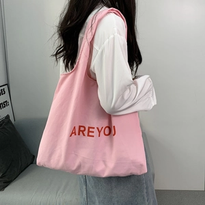 Detail of pink canvas tote bag with red AREYOU lettering worn by a model in a studio