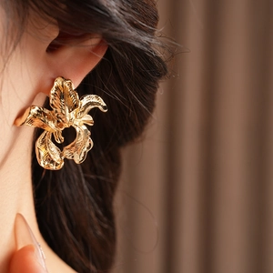 Close-up of golden irregular flower earrings on model highlighting metallic luster