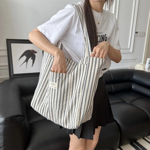 Blue and white striped canvas tote bag shown with exterior pocket in a home setting
