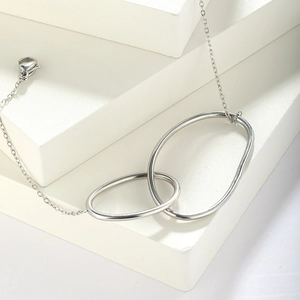 Minimalist silver stainless steel double circle bracelet on a modern white geometric stand