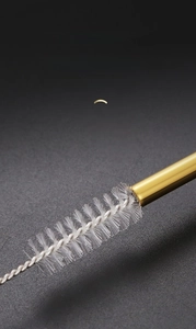 Macro view of cleaning pipe brush with white bristles entering a golden metal straw