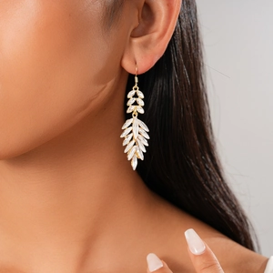 Close-up of gold leaf-shaped earring with white marquise crystals on model's ear