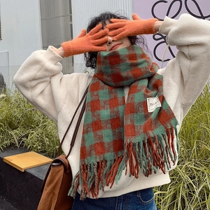 Outdoor lifestyle shot of a thick red and green plaid scarf with soft orange knit gloves