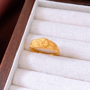 Détail macro d'une bague croix dorée à trois fleurs avec finition brossée sur boîte