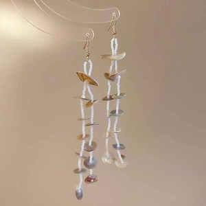 Detail of bohemian shell beads and gold hooks on long tassel earrings for beach style