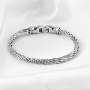 Detailed close-up of a silver stainless steel cable twisted bracelet on white silk