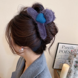 Close-up of a plush purple hair claw clip with a blue heart and pom-pom detail