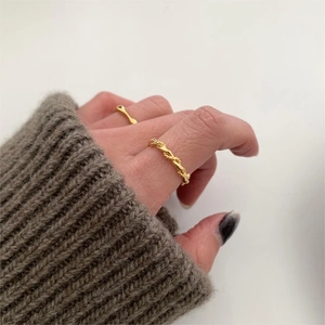 Detail of twisted rope gold ring worn on hand with cozy grey knit sweater background