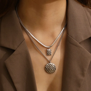 Detail of layered silver necklaces with square zircon and round hammered pendants on model