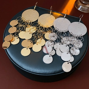 Macro shot of gold and silver metallic sequin tassel earrings on black display stand
