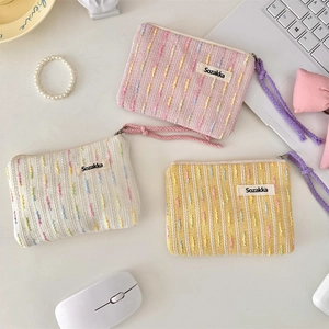 Close-up of woven makeup bags in pink, white, and yellow with braided cotton zipper pulls