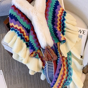 Ethnic knit poncho with faux fur collar and colorful tassels on grey armchair