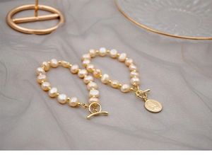 Detail of freshwater pearl bracelet with gold coin charm on elegant grey fabric