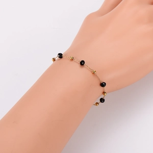 Bracelet chaîne dorée minimaliste avec perles noires facettées et boules d'or sur mannequin