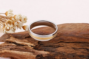 Détail d'une bague bicolore en acier inoxydable avec ligne dorée sur bois et fleurs blanches