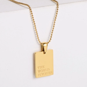 Gold beaded chain necklace with rectangle pendant engraved with THE WORLD IS YOURS