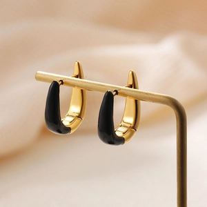 Macro detail of U-shaped gold earrings with black enamel finish on a metal display stand