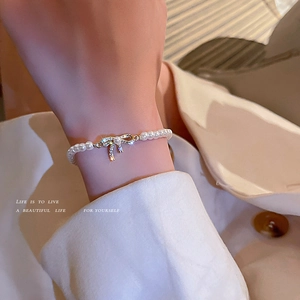 Elegant gold-plated pearl bracelet with a sparkling diamond bow charm on a female wrist