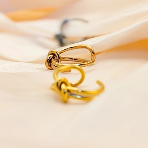 Macro shot of minimalist gold and silver knot rings on soft beige silk background