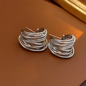 Close-up of silver C-shaped hoop earrings with multi-layer winding design on leather