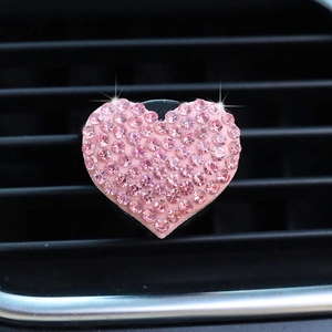 Macro view of a pink rhinestone heart-shaped car air vent clip in a car interior
