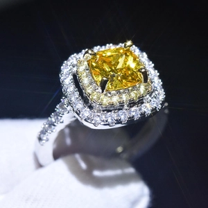 Macro shot of silver ring with yellow cushion cut stone and diamond halo on black background