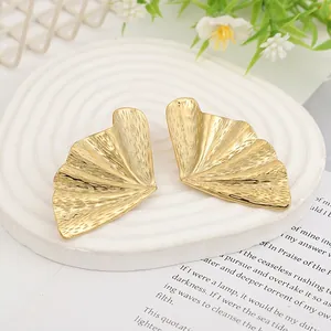 Detailed close-up of golden ginkgo leaf earrings with brushed metallic texture on tray