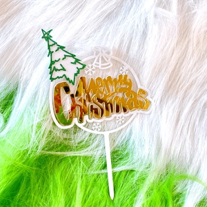 Close-up of a white acrylic Merry Christmas cake topper with a green glittery tree