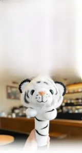 Close-up of plush tiger stick toy with blue button eyes and pink nose in soft material