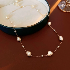 Detailed shot of irregular white pearls on a gold plated chain in a green jewelry dish