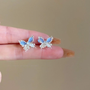 Vue rapprochée des boucles d'oreilles papillon avec cristaux dégradés bleus portées à la main