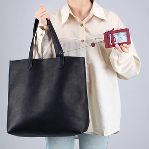Minimalist black leather tote bag with a red leather badge holder and lanyard