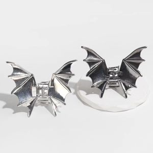 Close-up of bat wing shaped metal hair claws in silver and dark grey on white stand