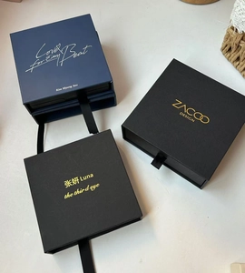 Detalle de cajas de regalo de lujo azul y negro con logo dorado y asas de cinta