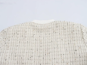 Gros plan sur la texture en tweed beige avec paillettes dorées et col rond côtelé blanc