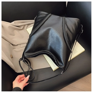 Detail of vintage black soft PU leather hobo bag with dual zipper design on a leather sofa