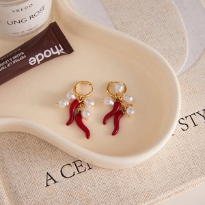 Eleganti orecchini a peperoncino rosso con perle e cerchi dorati su vassoio in ceramica