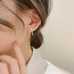 Detailed view of pearl earrings in an X-shaped cross design worn on a model ear
