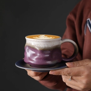 Close-up of handmade ceramic coffee cup with heart latte art and purple-blue gradient glaze