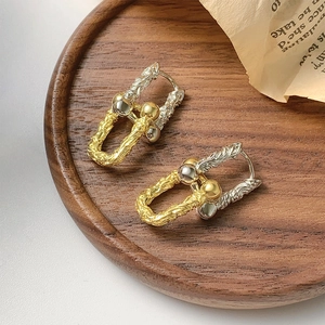 Two-tone horseshoe hoop earrings with twisted texture on a vintage wood tray background